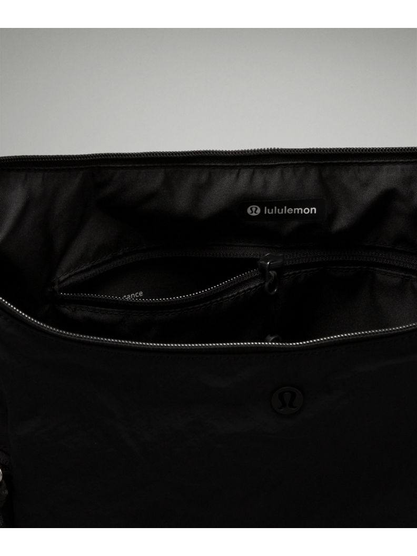 کیف اسلوچی اسلینگ 13 لیتری Lululemon، نمای نزدیک محفظه باز کیف مشکی، جیب زیپ‌دار و برچسب lululemon