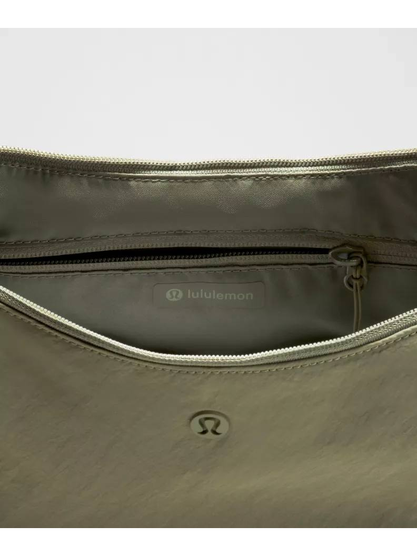 کیف اسلوچی اسلینگ 13 لیتری Lululemon، نمای نزدیک دهانه باز کیف زیتونی، جیب زیپ‌دار و نشان لولولمون