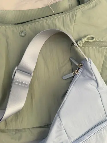 کیف اسلوچی اسلینگ 13 لیتری Lululemon، نمای نزدیک بند قابل‌تنظیم کیف آبی روشن، کنار کیف زیتونی