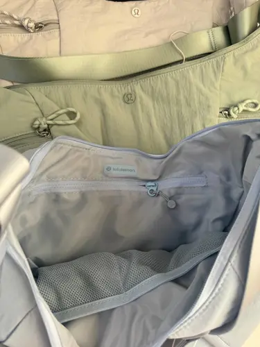 کیف اسلوچی اسلینگ 13 لیتری Lululemon، نمای محفظه باز کیف آبی روشن و جیب داخلی، کنار کیف زیتونی