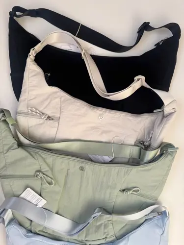 کیف اسلوچی اسلینگ 13 لیتری Lululemon، کیف‌های اسلینگ مشکی، کرم، زیتونی و آبی روشن کنار هم روی سطح روشن