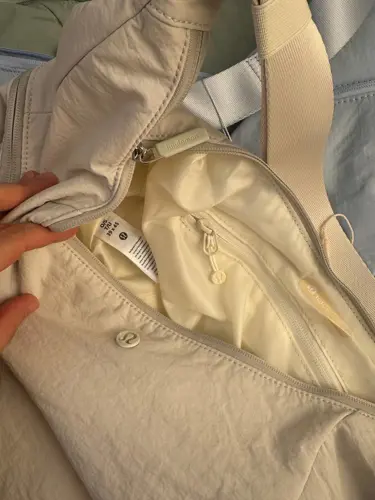 کیف اسلوچی اسلینگ 13 لیتری Lululemon، نمای نزدیک محفظه باز و آستر کرم کیف اسلینگ در دست