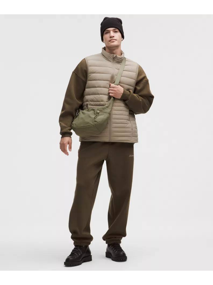 کیف اسلوچی اسلینگ 13 لیتری Lululemon، کیف اسلینگ زیتونی به‌صورت مورب روی مدل با جلیقه کرم، شلوار قهوه‌ای و کلاه تیره