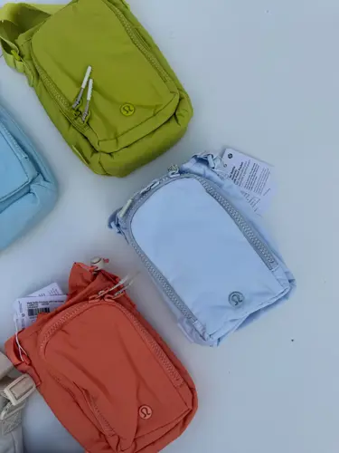 باتل بگ اورجینال Lululemon، کیف‌های بنددار آبی، سبز لیمویی، نارنجی، زرشکی و کرم روی زمینه روشن