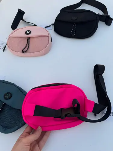 بلت بگ کرو Lululemon، کیف‌های بیضی مشکی، صورتی و آبی تیره با بند و سگک پهن، روی زمینه روشن