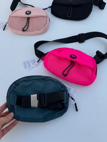 بلت بگ کرو Lululemon، کیف‌های بیضی مشکی، صورتی و آبی تیره با بند و سگک پهن، روی زمینه روشن