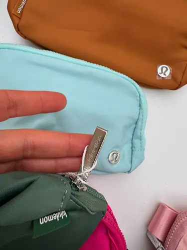 بلت بگ Lululemon، نمای نزدیک سرزیپ فلزی کیف سبز در دست، کنار کیف آبی روشن