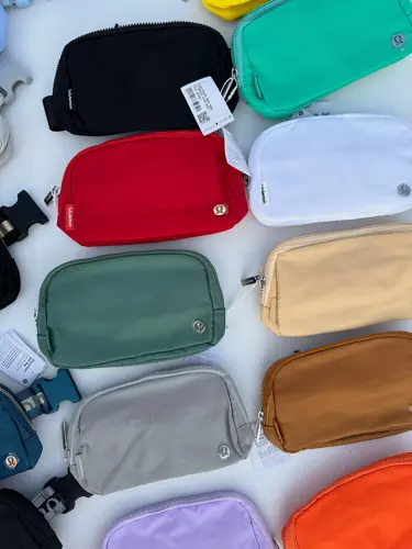 بلت بگ Lululemon، چیدمان کیف‌های کمری رنگارنگ با زیپ و نشان لولولمون، روی زمینه روشن