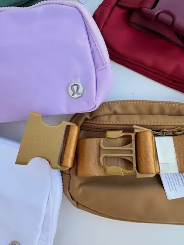 بلت بگ Lululemon، کیف‌های یاسی، زرشکی و قهوه‌ای با نشان لولولمون و سگک پهن، روی زمینه روشن