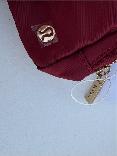 بلت بگ وردمارک Lululemon، زرشکی؛ نمای نزدیک نشان فلزی لولولمون و دوخت گوشه کیف