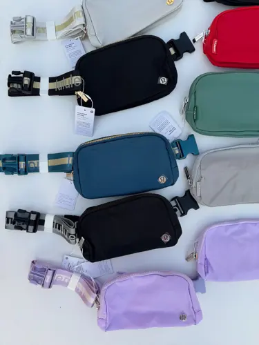 بلت بگ وردمارک Lululemon، چیدمان کیف‌های کمری رنگی با بندهای نوشته‌دار و سگک، روی زمینه روشن
