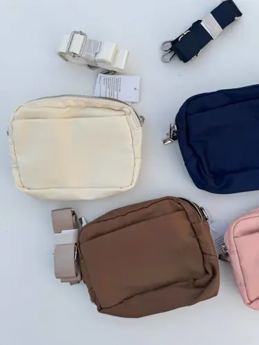 کیف ساید سینچ Lululemon، کیف‌های مستطیلی کرم، سرمه‌ای و قهوه‌ای با بندهای قابل‌تنظیم روی سطح سفید