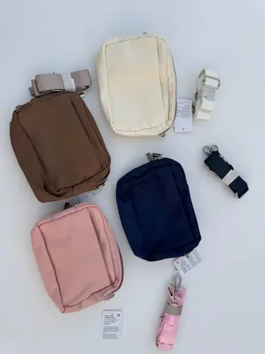 کیف ساید سینچ Lululemon، کیف‌های کرم، قهوه‌ای، سرمه‌ای و صورتی با بندهای جدا و زیپ فلزی روی سطح سفید