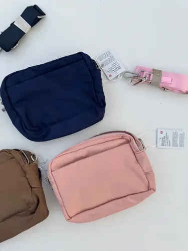 کیف ساید سینچ Lululemon، کیف‌های مستطیلی سرمه‌ای، صورتی و قهوه‌ای با بندهای جدا روی سطح سفید
