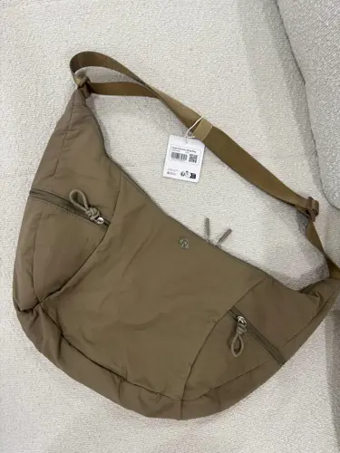 کیف اسلوچی اسلینگ 13 لیتری Lululemon، کیف اسلینگ زیتونی با جیب بیرونی و بند بلند روی سطح روشن - تصویر دوم