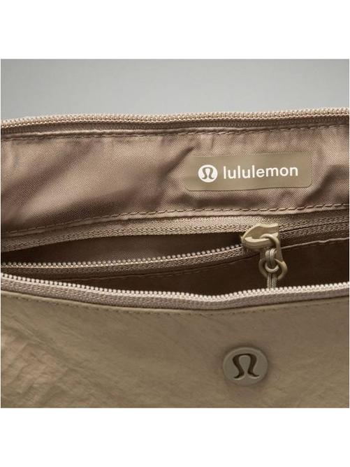کیف اسلوچی اسلینگ 13 لیتری Lululemon، نمای نزدیک جیب زیپ‌دار و نوشته lululemon داخل کیف زیتونی