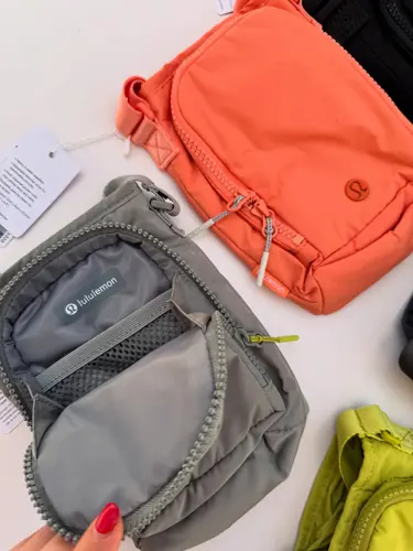 باتل بگ اورجینال Lululemon، کیف خاکستری باز با جیب توری داخل، کنار کیف نارنجی روی زمینه روشن