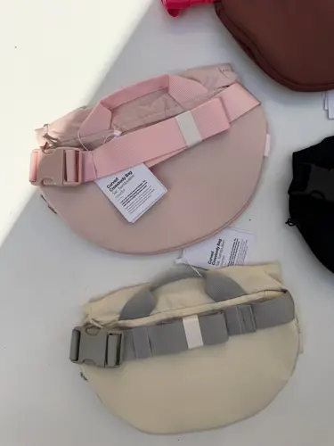 بلت بگ 3 لیتری Lululemon، پشت کیف‌های صورتی و کرم با بند و سگک پهن، روی زمینه روشن