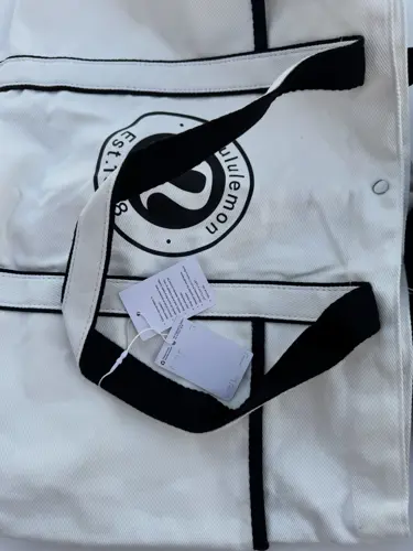 توت بگ کتان Lululemon، سفید با خطوط و لوگوی گرد مشکی؛ دسته‌های مشکی روی کیف