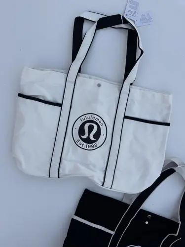 توت بگ کتان Lululemon، دو توت‌بگ سفید و مشکی با خطوط متضاد و لوگوی گرد لولولمون، روی زمینه روشن