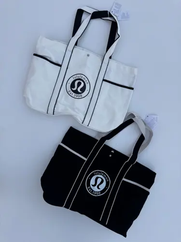 توت بگ کتان Lululemon، دو توت‌بگ سفید و مشکی با خطوط متضاد و لوگوی گرد لولولمون، روی زمینه روشن - تصویر دوم