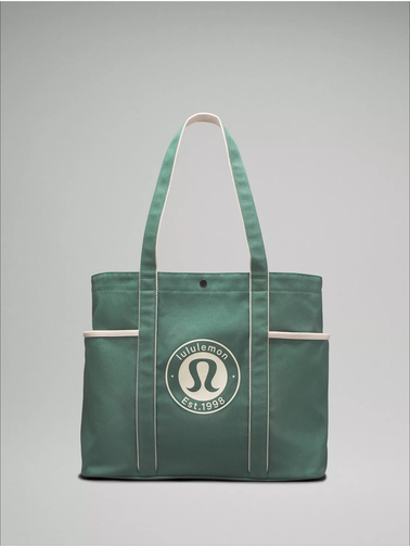 توت بگ کتان Lululemon، سبز با خطوط سفید و لوگوی گرد لولولمون؛ از جلو روی زمینه روشن