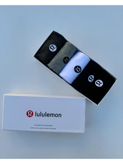 جوراب ساقدار Lululemon، جوراب‌های مشکی، خاکستری و سفید رول‌شده در جعبه باز، کنار در سفید با لوگوی lululemon