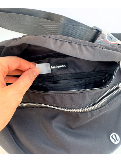کراس بادی نورلاست Lululemon، نمای نزدیک داخل کیف مشکی، جیب زیپ‌دار و برچسب داخلی در دست