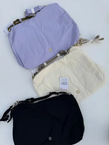 کراس بادی کانورتیبل Lululemon، کیف‌های بنفش روشن، کرم و مشکی با بندهای کوتاه و یراق طلایی روی سطح سفید