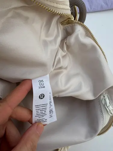 کراس بادی کانورتیبل Lululemon، نمای نزدیک برچسب سفید داخل کیف کرم با زیپ طلایی باز در دست