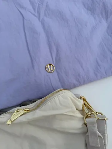 کراس بادی کانورتیبل Lululemon، نمای نزدیک لوگوی طلایی روی کیف بنفش روشن و زیپ طلایی کیف کرم - تصویر دوم