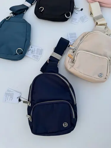 کیف اسمال اسلینگ Lululemon، کیف‌های تک‌بند مشکی، سرمه‌ای، آبی تیره، صورتی و کرم با جیب زیپ‌دار، روی زمینه روشن