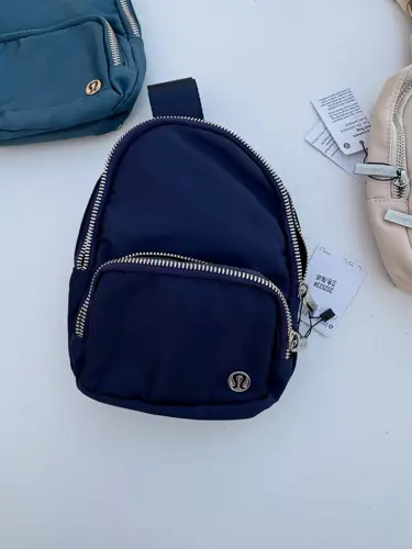 کیف اسمال اسلینگ Lululemon، سرمه‌ای با بند پهن و جیب زیپ‌دار، روی زمینه روشن