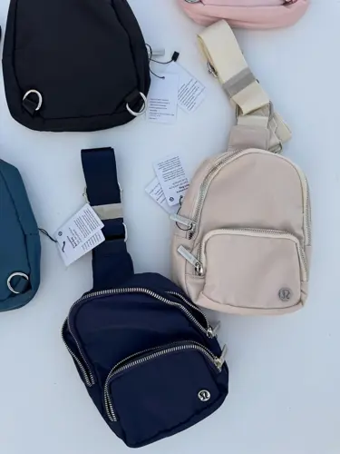 کیف اسمال اسلینگ Lululemon، کیف‌های تک‌بند مشکی، سرمه‌ای، آبی تیره، صورتی و کرم با جیب زیپ‌دار، روی زمینه روشن