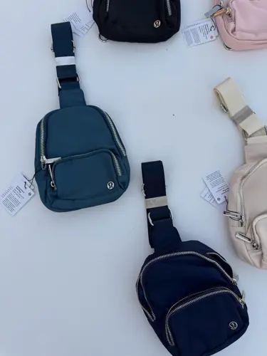 کیف اسمال اسلینگ Lululemon، کیف‌های تک‌بند مشکی، سرمه‌ای، آبی تیره، صورتی و کرم با جیب زیپ‌دار، روی زمینه روشن