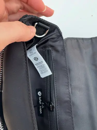 کیف دوشی مولتی پاکت Lululemon، مشکی؛ نمای نزدیک حلقه بند و برچسب داخل کیف