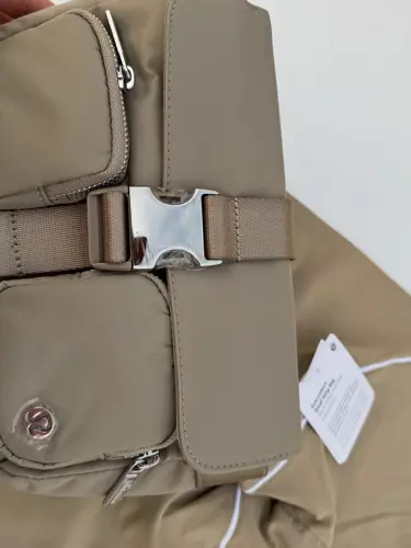 کیف دوشی مولتی پاکت Lululemon، بژ با دو جیب زیپ‌دار و سگک فلزی وسط؛ روی لباس بژ