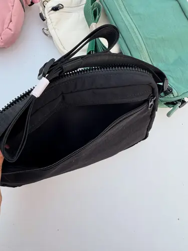 کراس بادی مولتی پاکت Lululemon، مشکی؛ نمای نزدیک محفظه باز و آستر کیف، کنار کیف سبز