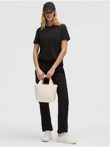 کیف مینی توت بگ Lululemon، کیف مینی کرم در دست مدل با تیشرت و شلوار مشکی، کلاه تیره و کفش سفید