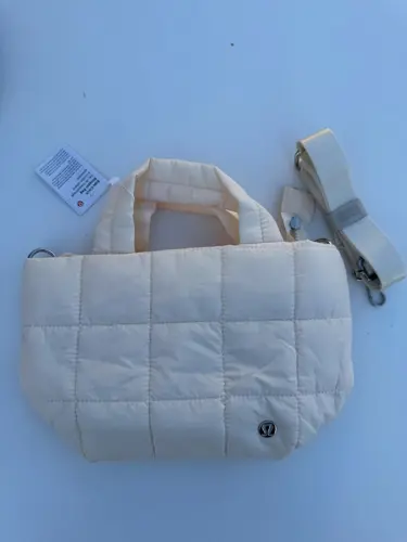 کیف مینی توت بگ Lululemon، کیف مینی کرم با دوخت مربعی، دسته‌های کوتاه و لوگوی فلزی روی سطح آبی روشن - تصویر اصلی