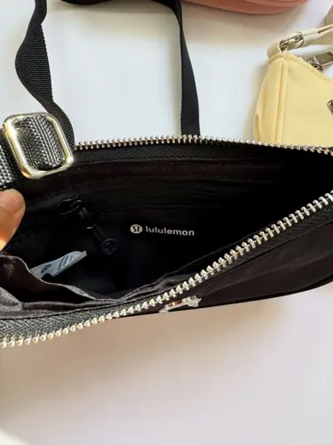 کیف مینی شولدر Lululemon، نمای داخل کیف مشکی با زیپ طلایی باز، در دست و کنار کیف زرد روشن