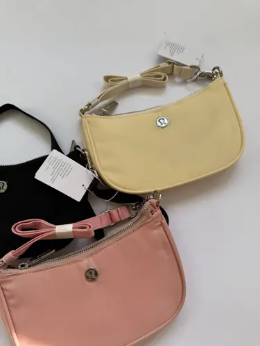 کیف مینی شولدر Lululemon، کیف‌های مینی مشکی، صورتی هلویی و زرد روشن با دسته کوتاه و لوگوی فلزی روی سطح روشن