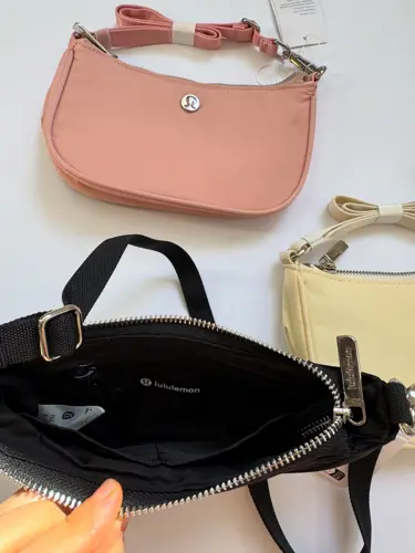 کیف مینی شولدر Lululemon، کیف صورتی هلویی بالای کیف مشکی با زیپ باز در دست؛ کیف زرد روشن در کنار آن‌ها