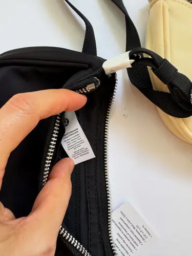 کیف مینی شولدر Lululemon، نمای نزدیک برچسب داخلی کیف مشکی کنار زیپ، در دست