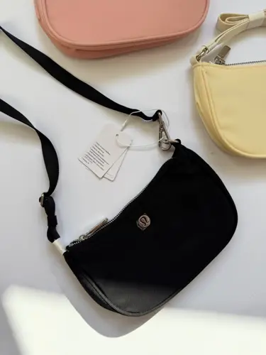 کیف مینی شولدر Lululemon، نمای نزدیک کیف مینی مشکی با دسته کوتاه و لوگوی فلزی روی سطح روشن - تصویر دوم