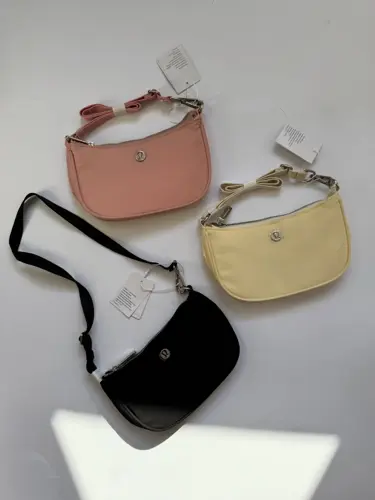 کیف مینی شولدر Lululemon، کیف‌های مینی مشکی، صورتی هلویی و زرد روشن با دسته کوتاه و لوگوی فلزی روی سطح روشن - تصویر اصلی