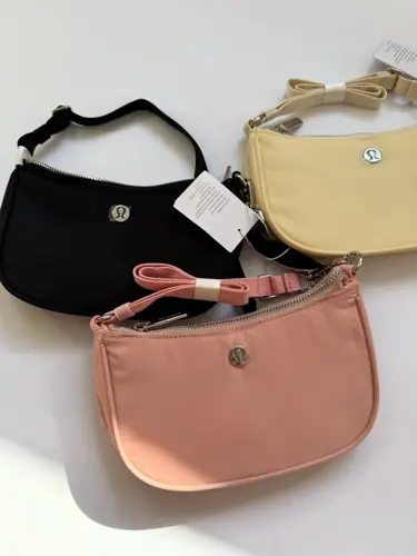 کیف مینی شولدر Lululemon، کیف‌های مینی مشکی، صورتی هلویی و زرد روشن با دسته کوتاه و لوگوی فلزی روی سطح روشن