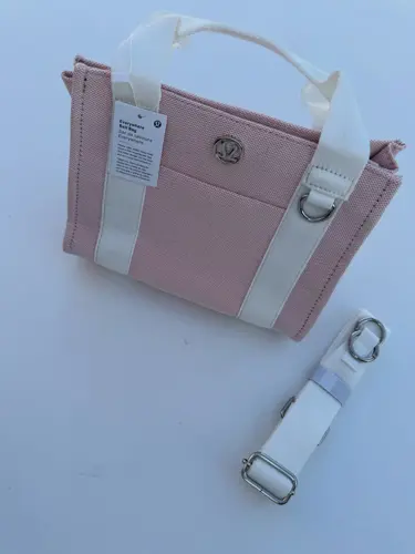 کیف کانواس Lululemon، صورتی روشن با دسته و نوارهای سفید، نشان فلزی لولولمون و بند جداشونده، روی زمینه روشن
