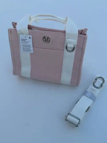 کیف کانواس Lululemon، صورتی روشن با دسته و نوارهای سفید، نشان فلزی لولولمون و بند جداشونده، روی زمینه روشن - تصویر اصلی