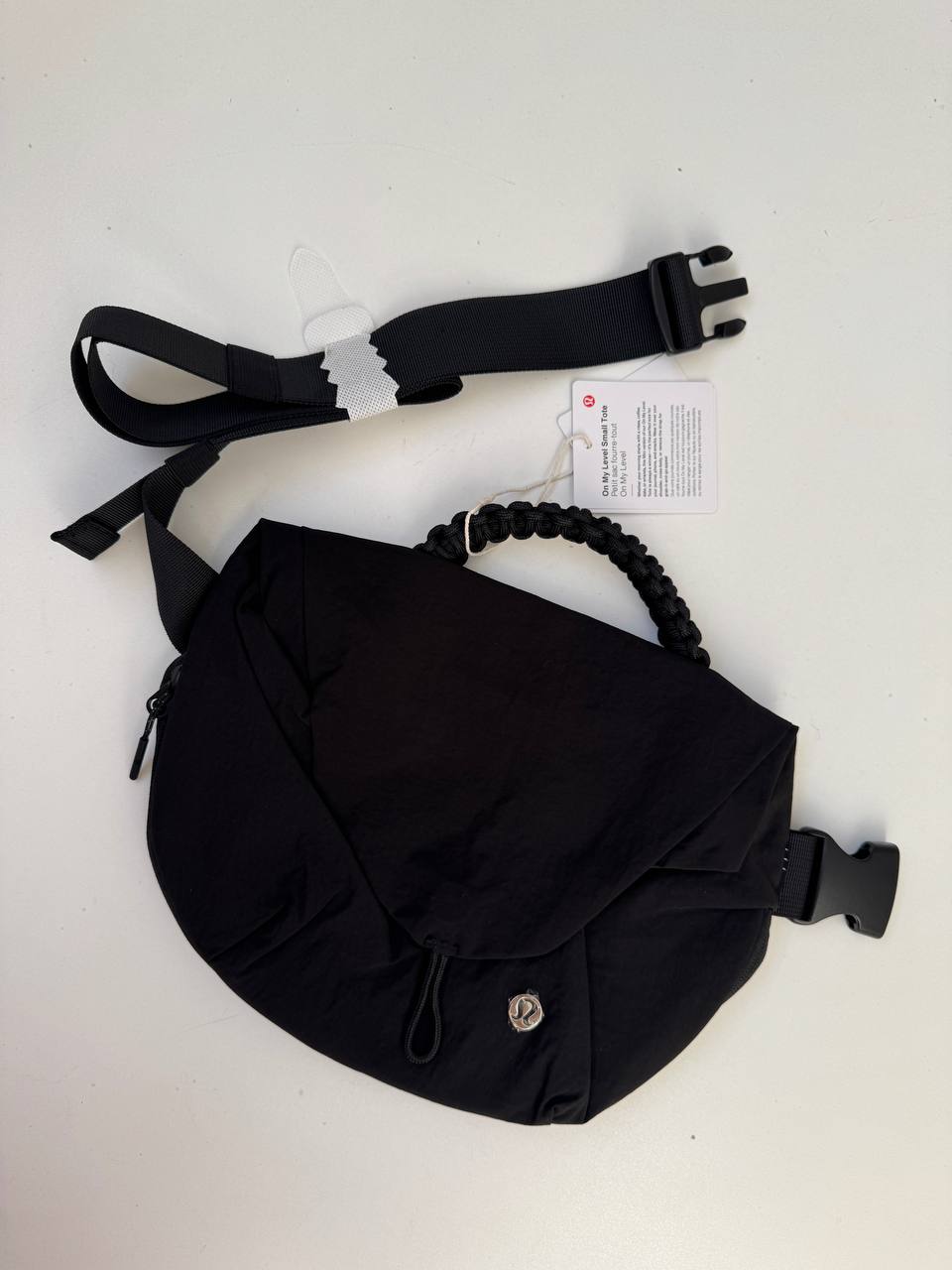 بلت بگ 3 لیتری Lululemon، کیف کمری مشکی با دسته بافته‌شده و بند سگک‌دار جداشده روی سطح روشن